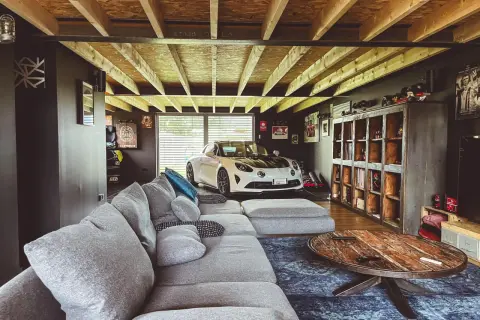 Aménager son garage : un canapé confortable, une voiture de sport blanche et des étagères remplies d'objets de collection.
