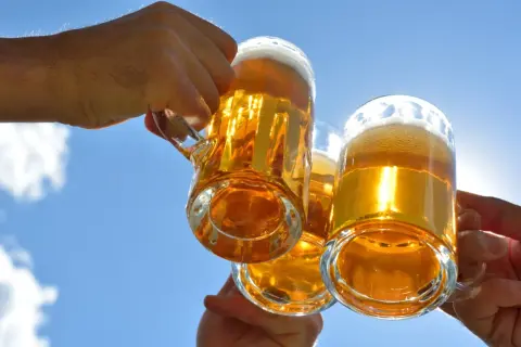 Trzy kufle piwa Żubr wzniesione do toastu pod błękitnym niebem. Ile cukru ma piwo Żubr?