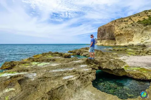 Hombre contempla el mar azul desde las rocas cerca del faro de Cabo de Gata. Acantilados y aguas cristalinas.
