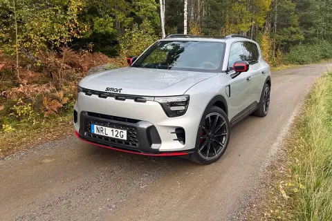 En smart 5-dörrars SUV i silver med röda detaljer kör på en grusväg genom en höstskog.