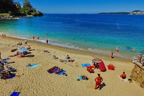 Gente disfrutando del sol y el mar en la playa Portocelo. Arena dorada, aguas turquesas y un día perfecto para relajarse.