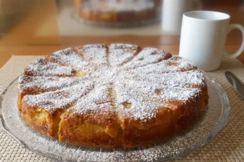 Gâteau fondant aux pommes et mascarpone, saupoudré de sucre glace, prêt à être dégusté avec une tasse de café.