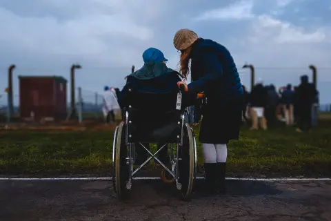 Donna assiste persona in sedia a rotelle, un momento di cura che ricorda l'importanza dell'indennità di accompagnamento dopo i 18 anni.
