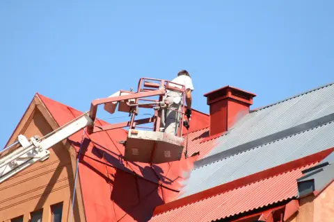 Pracownik na podnośniku maluje czerwony dach. Sprawdź, jaka jest malowanie dachu cena i odśwież wygląd swojego domu.
