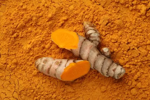 Intensywny pomarańczowy proszek z kurkumy, z widocznymi kawałkami korzenia. To naturalne składniki, które od wieków wykorzystuje się w kosmetyce.