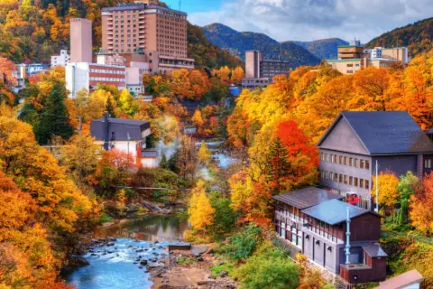 Town nestled in a valley with a river, surrounded by trees in vibrant autumn colors.