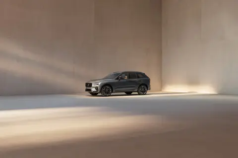 En mörkgrå Volvo XC60 står i ett ljust, minimalistiskt rum. Bilen visar upp sina eleganta linjer och fälgar, en perfekt representation av Volvo utrustningsnivåer.