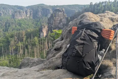 Rucksack und Wanderstöcke auf Felsen mit Bergpanorama. Alles pvc frei für umweltbewusstes Trekking.