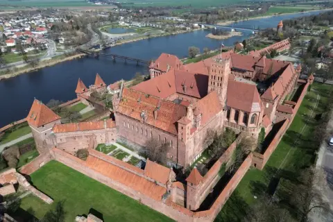 Potężny zamek w Malborku, największy zamek w Europie, rozciąga się wzdłuż rzeki. Jego ceglane mury i wieże świadczą o bogatej historii.
