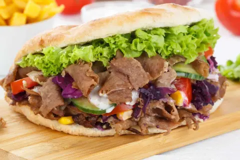Un généreux kebab maison garni de viande, salade, tomates, concombre et chou rouge, prêt à être dégusté.