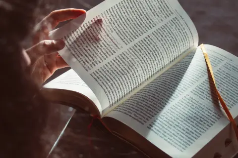 Osoba czyta Biblię, zgłębiając dogmaty wiary katolickiej. Światło podkreśla tekst, symbolizując oświecenie.