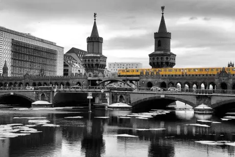 Gelbe U-Bahn fährt über die Oberbaumbrücke in Berlin. Im Vordergrund treibt Eis auf dem Wasser.