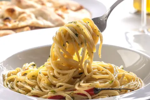 Widok z bliska na talerz pysznego, smażonego makaronu spaghetti z ziołami i kawałkami papryczki chili. Na drugim planie widać pieczywo.