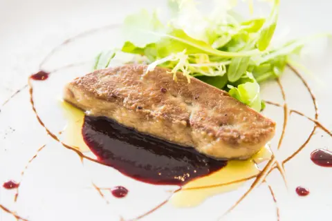 Un morceau de foie gras poêlé, servi avec une sauce aux fruits rouges et une salade verte. Une recette raffinée pour un plat d'exception.