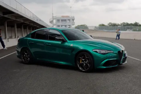 Zielona Alfa Romeo Giulia Quadrifoglio na torze wyścigowym, z wieżą kontrolną w tle.