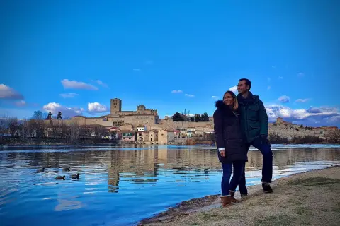 Pareja disfruta de la vista del río Duero y la ciudad de Zamora, un lugar que merece la pena visitar. Patos nadan en el agua azul.