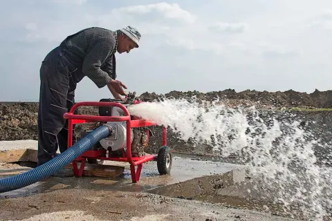 Hombre trabajando con una bomba de agua que lanza un chorro potente. A pesar de que se puede andar con la bomba de agua rota, él la mantiene en funcionamiento.