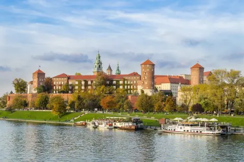 Zabytkowe miasto nad Wisłą, Wawel w jesiennej odsłonie, z łodziami cumującymi przy brzegu.