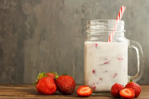 Kefir z truskawkami w słoiku z uchem, obok świeże truskawki na drewnianym stole.