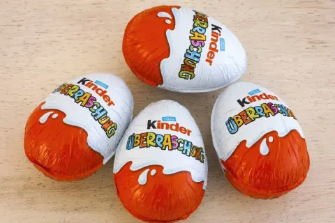 Cztery jajka Kinder Niespodzianka na drewnianym tle.