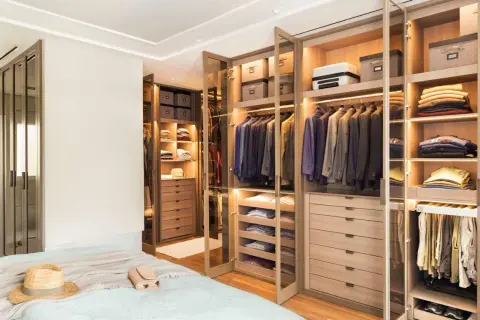 Armarios a medida con puertas de cristal y madera, llenos de trajes, ropa doblada y accesorios.