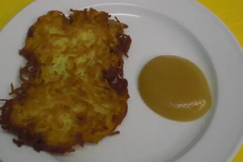 Zwei knusprige Kartoffelpuffer liegen auf einem Teller neben einem Klecks Apfelmus.