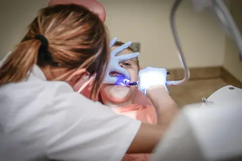 Dentysta z niebieskim światłem bada zęby dziecka.