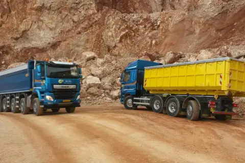 Deux camions bleus, un avec une benne jaune, circulent sur un chemin de carrière. Le prix du km camion 26 tonnes est une donnée clé pour ces transports.