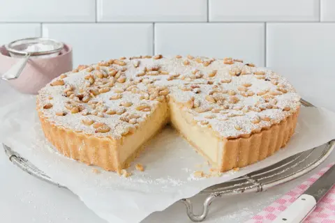 Eine köstliche Torta della Nonna, bestäubt mit Puderzucker und Pinienkernen, wartet darauf, angeschnitten zu werden.