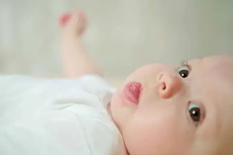 Un bébé aux yeux curieux sort sa langue, un geste innocent dont la signification peut varier.