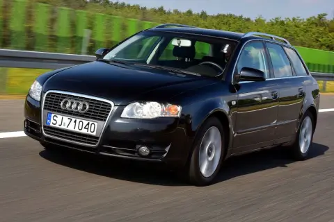 Czarne Audi A4 B7 2.0 TDI na autostradzie, z zielonymi barierami i drzewami w tle.