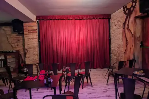 El escenario de el.sotano magico, con cortinas rojas y sillas metálicas, listo para un espectáculo.