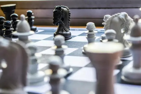 Czarny koń na szachownicy, gotowy do wykonania swojego charakterystycznego ruchu, jak porusza się koń w szachach.