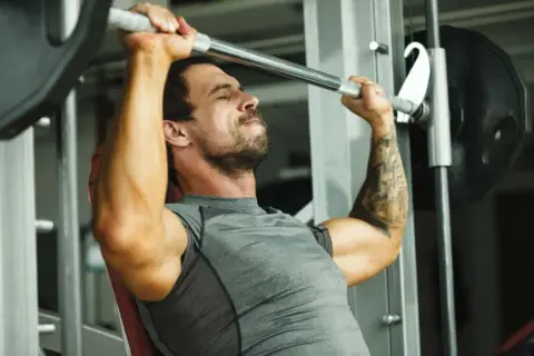 Mann hebt mit konzentriertem Gesichtsausdruck eine Langhantel im Fitnessstudio, ein intensiver 1 satz training.