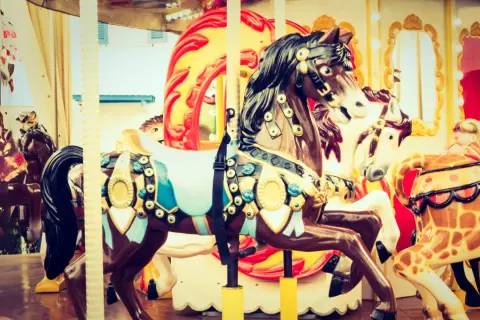 Chevaux décorés sur un manège de fête foraine, avec des touches de roses dans les ornements et les lumières.