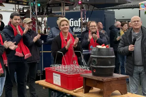 Menschen mit roten Schals klatschen bei Ruppichteroth Veranstaltungen. Eine Frau mit blonden Haaren steht im Mittelpunkt, daneben ein Mann mit Mikrofon.