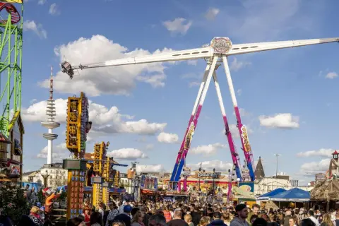 Voller Rummelplatz mit Achterbahn, einem riesigen Pendel und vielen Menschen. Im Hintergrund ragt der Hamburger Fernsehturm auf.