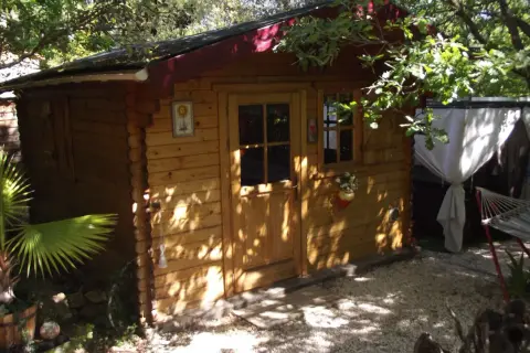 Charmante cabane en bois, nichée sous les arbres. Un hamac invite à la détente à côté.