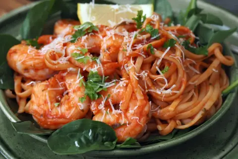 En skål med pasta pomodoro med räkor, toppad med riven ost och färsk persilja. En citronklyfta vilar ovanpå.