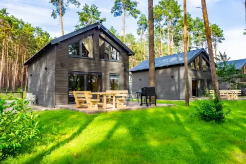 Nowoczesne lubiatów domki nad jeziorem w otoczeniu sosnowego lasu. Drewniane meble i grill zapraszają do relaksu.