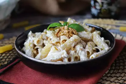 Makaron penne z kremowym sosem, orzechami włoskimi i bazylią w czarnej misce.