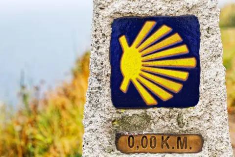 Das Jakobsweg Symbol Bedeutung: Eine gelbe Muschel auf blauem Grund, die den Beginn der Pilgerreise markiert. 0,00 km.