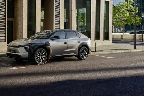 En silverfärgad elbil laddas vid en modern byggnad. En fråga som många ställer sig är: vad kostar det att ladda en hybridbil?