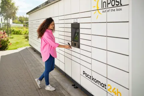 Kobieta z telefonem przy Paczkomacie InPost. Szybka wysyłka paczek za granicę jest teraz prosta.