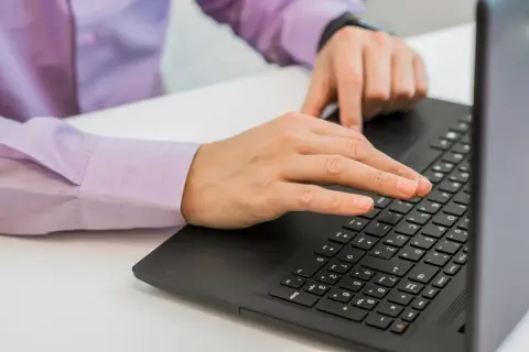 Dłonie piszące na klawiaturze laptopa.