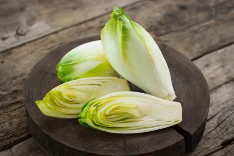 Frische Chicorée-Köpfe, einer davon halbiert, liegen auf einem Holzbrett. Perfekt für einen knackigen Chicorée-Salat.