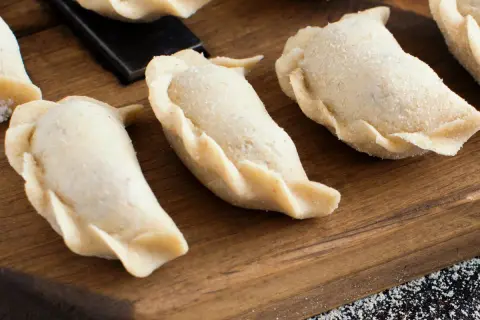 Surowe pierogi na desce. Zastanawiasz się, ile gotować pierogi, by były idealne?
