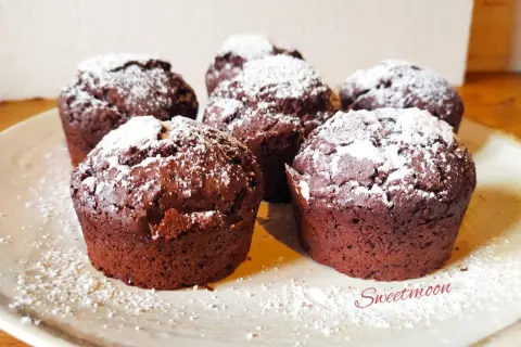 Cinque muffin al cioccolato senza burro, spolverati di zucchero a velo, su un piatto chiaro.