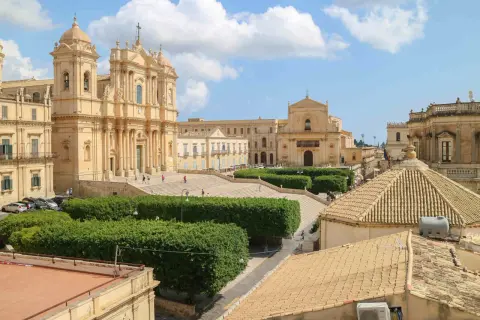 Piazza barocca con chiese imponenti e giardini curati, un esempio di città d'arte Italia sotto un cielo azzurro con nuvole bianche.