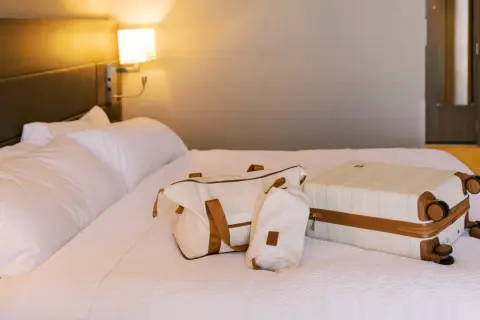 Biała walizka i torba podróżna na łóżku w hotelu.